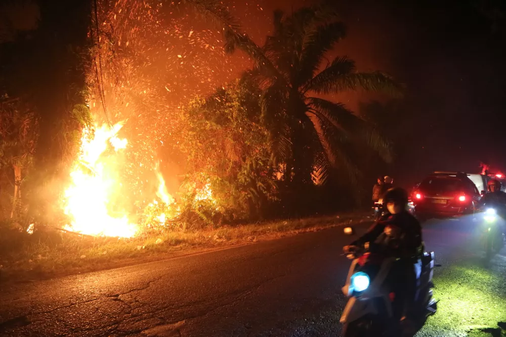 Motorists ride past a wildfire burning through a peatland field in Sampit, Central Kalimantan, Indonesia, Monday, Aug. 24, 2026. (AP Photo/Andri Rizky Agustian)