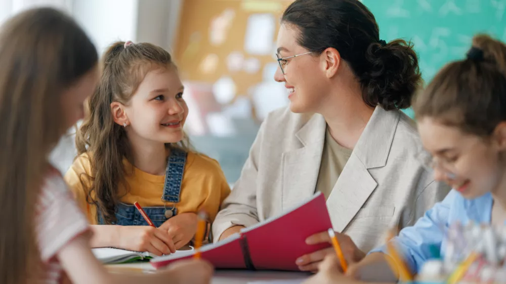 Happy kids and teacher at school. Woman and children are working in the class.