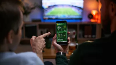 Young adult men watching football match and checking betting app on smartphone, expressing male friendship and shared leisure. Useful for sports betting, gaming, entertainment marketing