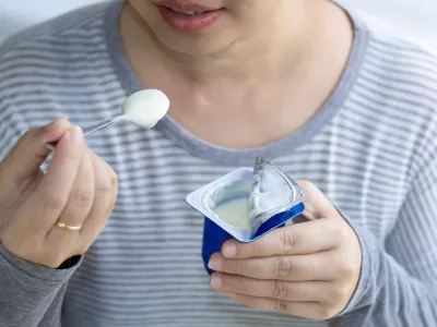 Beautiful woman eating yogurt in the morning, her hand holding a cup of yogurt and a spoon. Yogurt made from milk fermented by added bacteria, often sweetened and flavored. selective focus. / Foto: Pong-photo9 Getty Images