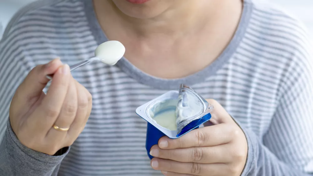 Beautiful woman eating yogurt in the morning, her hand holding a cup of yogurt and a spoon. Yogurt made from milk fermented by added bacteria, often sweetened and flavored. selective focus. / Foto: Pong-photo9 Getty Images