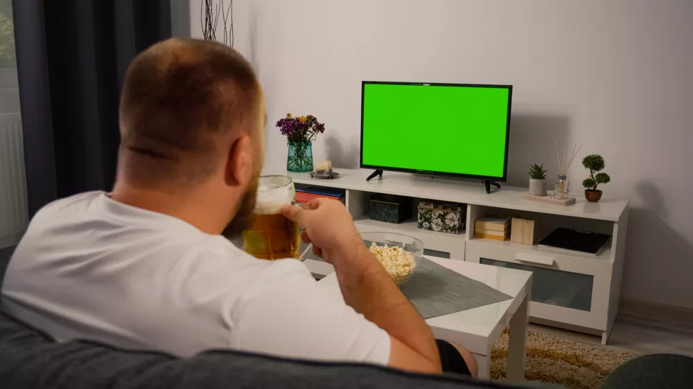 Man Watching Green Screen TV at home. Drink Beer Eating Popcorn. Over the Shoulder Back view. Chroma key.