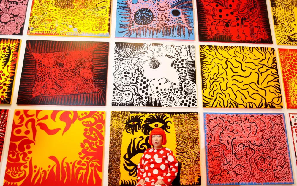 FILE - Japanese artist Yayoi Kusama poses for photographers in front of her painting 'Love Arrives at the Earth Carrying with it a Tale of the Cosmos', center bottom, and other paintings at the Tate Modern in London, Tuesday, Feb. 7, 2012.(AP Photo/Kirsty Wigglesworth, File)