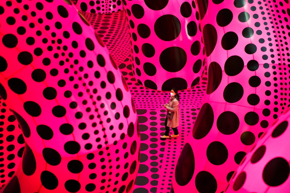 FILE - A woman walks through the art work 'A Bouquet of Love I Saw in the Universe' by Yayoi Kusama during the press preview of a retrospective exhibition of the Japanese artist at the Martin Gropius Bau museum in Berlin, Germany, Thursday, April 22, 2021. (AP Photo/Markus Schreiber, File)