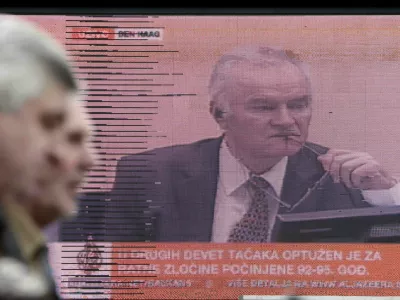 Bosnian people walking in a street pass a television screen in Sarajevo, Bosnia, on Wednesday, May 16, 2012 during a live TV broadcast as charges are read in court against Bosnian Serb Gen. Ratko Mladic at the U.N.'s Yugoslav war crimes tribunal in The Hague, Netherlands. Twenty years after Serb forces unleashed a brutal campaign of ethnic cleansing in Bosnia, their military commander Gen. Ratko Mladic is on trial Wednesday May 16, 2012, on charges of masterminding atrocities throughout the country devastating 1992-95 war.(AP photo/Amel Emric)