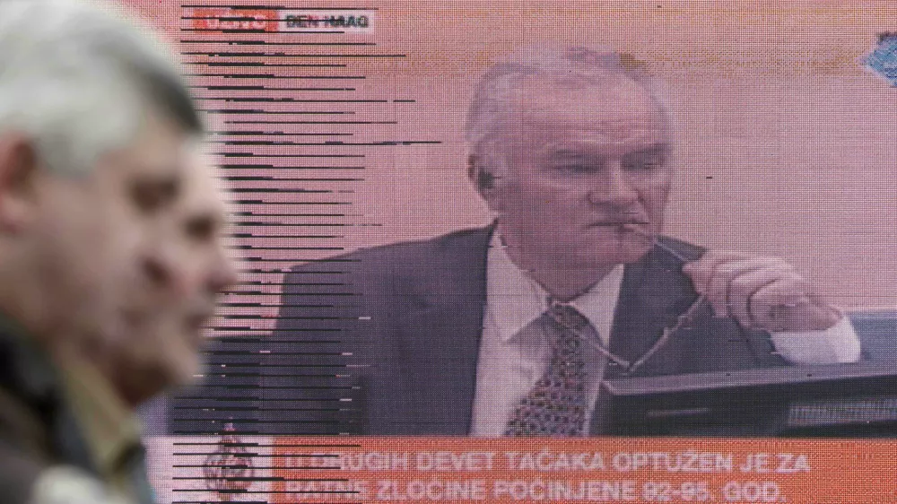 Bosnian people walking in a street pass a television screen in Sarajevo, Bosnia, on Wednesday, May 16, 2012 during a live TV broadcast as charges are read in court against Bosnian Serb Gen. Ratko Mladic at the U.N.'s Yugoslav war crimes tribunal in The Hague, Netherlands. Twenty years after Serb forces unleashed a brutal campaign of ethnic cleansing in Bosnia, their military commander Gen. Ratko Mladic is on trial Wednesday May 16, 2012, on charges of masterminding atrocities throughout the country devastating 1992-95 war.(AP photo/Amel Emric)