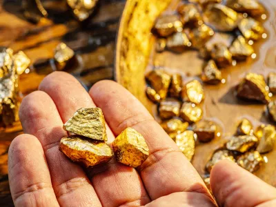 Gold nuggets on a brass plate and on palm. Imitation gold nuggets.