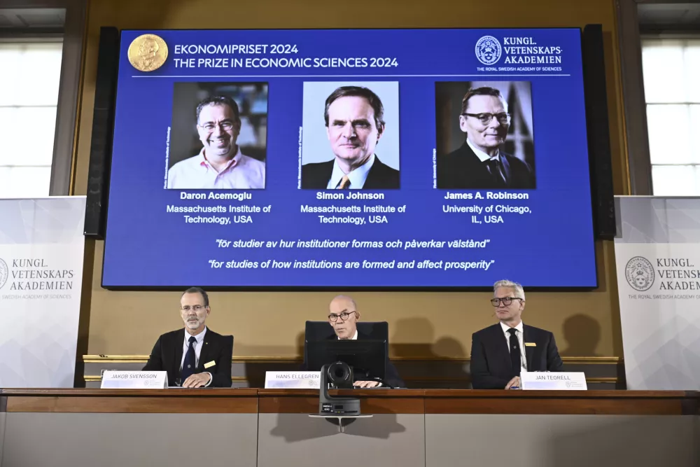 Academy of Sciences permanent secretary Hans Ellegren, center, Jakob Svensson, left, and Jan Teorell, of the Nobel assembly announce the Nobel memorial prize in economics winners, Daron Acemoglu, Simon Johnson and James A Robinson, seen on screen, during a press meeting at the Royal Swedish Academy of Sciences in Stockholm, Sweden, Monday Oct. 14, 2024. (Christine Olsson/TT News Agency via AP) / Foto: Christine Olsson