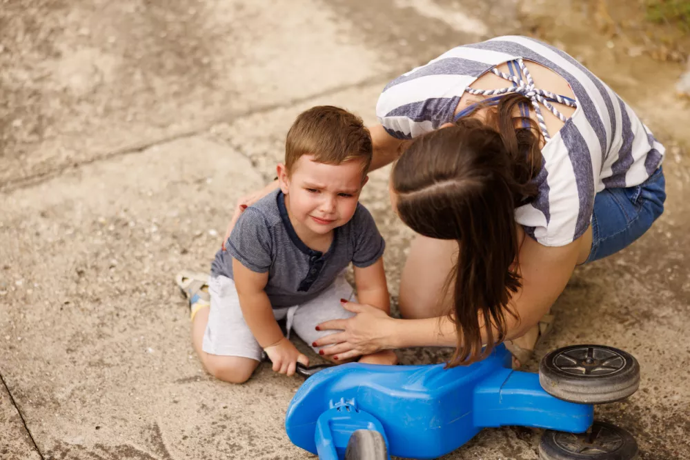 High angle view of mother comforting toddler son as he cries after falling off the bike while playing in the backyard