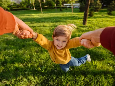 Smiling young boy holding hands with father while spinning playfully in a grassy park on a sunny day, full of excitement. Happy child portrait in movement during playtime. POV view