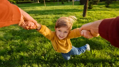 Smiling young boy holding hands with father while spinning playfully in a grassy park on a sunny day, full of excitement. Happy child portrait in movement during playtime. POV view