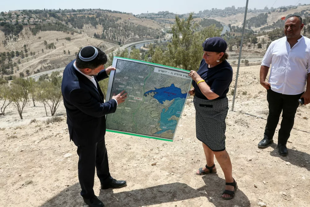 Israeli Finance Minister Bezalel Smotrich and a woman hold a map that shows the long-frozen E1 settlement scheme, that would split East Jerusalem from the occupied West Bank, on the day of a press conference near the Israeli settlement of Maale Adumim, in the Israeli-occupied West Bank, August 14, 2025. REUTERS/Ronen Zvulun