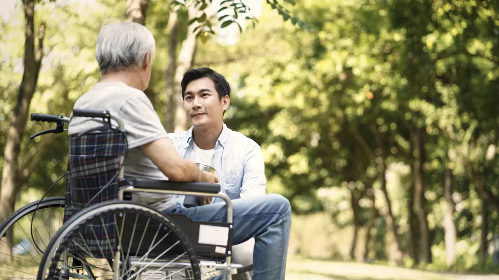 asian son talking to and comforting wheelchair bound father