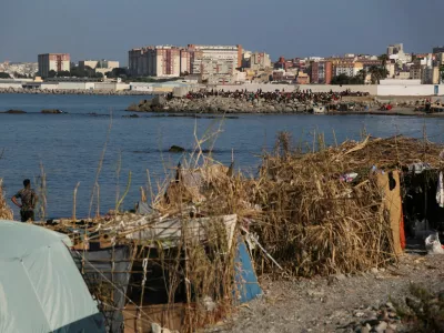 Makeshift shelters used by migrants line the coast as a crowd gathers on a breakwater in Ceuta, Spain, August 15, 2026. REUTERS/Maria Alejandra Cardona