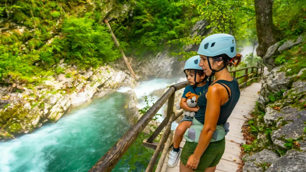Mother carrying her child while wearing helmets and observing the radovna river flowing through the scenic vintgar gorge near bled, slovenia