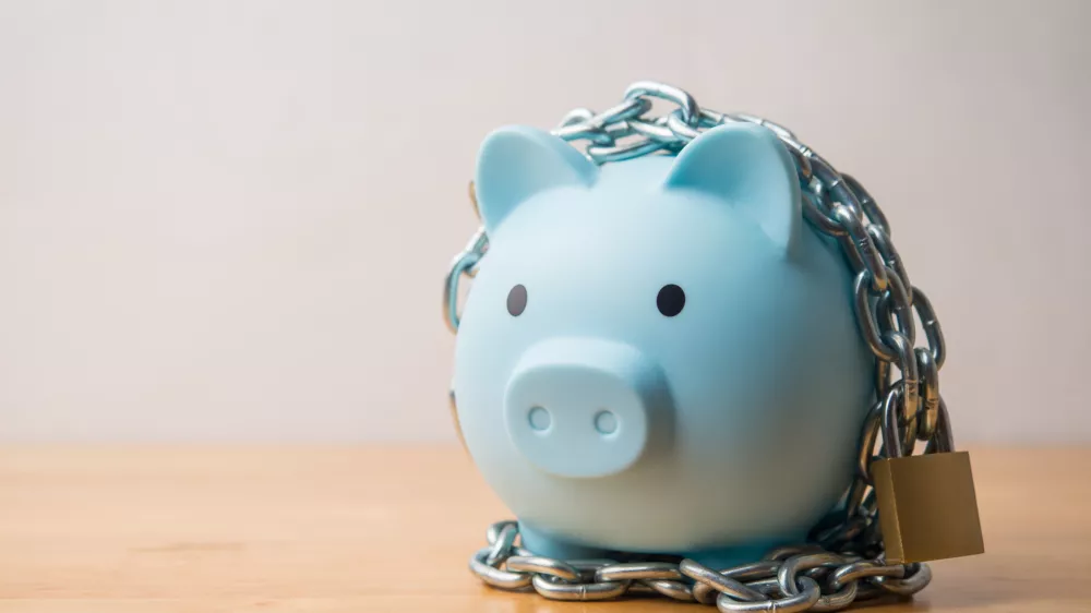Blue piggy bank locked with chain and padlock on wooden table white wall background. Savings money protection, money management, scammer prevention, safety deposit account, financial, economy concept.