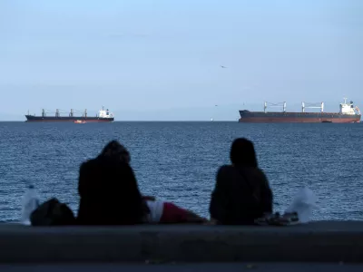 FILE - People sit in front of cargo ships anchor in the Marmara Sea await to cross the Bosphorus Straits in Istanbul, Turkey, on July 13, 2022. (AP Photo/Khalil Hamra, File)