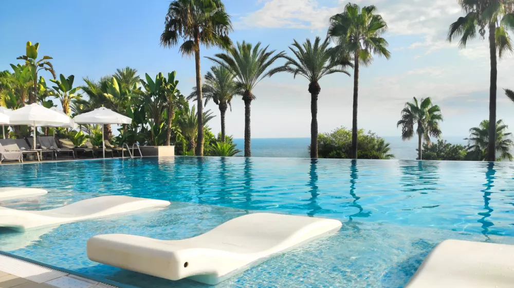 Stunning resort pool, surrounded by loungers, palms, and ocean views, is perfect for a getaway