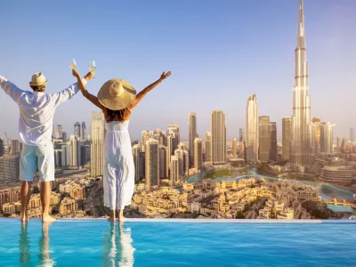 A happy tourist couple on vacation time stands by the pool edge and enjoys the panoramic sunset view of the Dubai city skyline, UAE