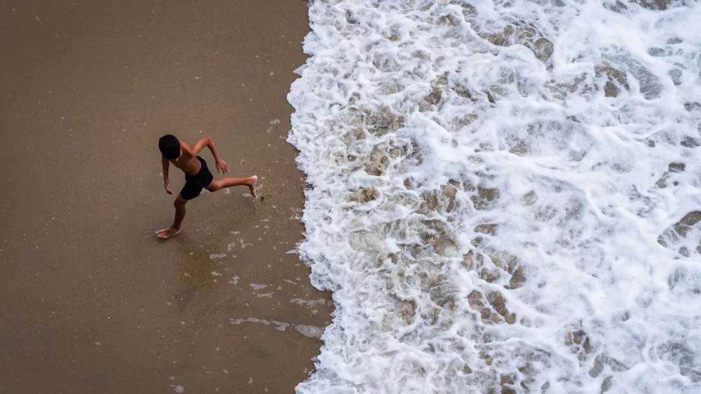 A child runs from the water as large waves from Hurricane Marie break on the shore, Monday, Sept. 7, 2026, on Huntington Beach, southern Calif. (AP Photo/Ethan Swope)