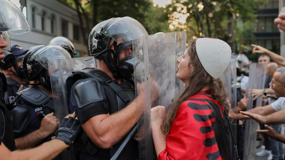 A woman draped in an Albanian flag clashes with police officers during ongoing demonstrations against plans for a luxury resort in a protected coastal area linked to Jared Kushner, U.S. President Donald Trump's son-in-law, in Tirana, Albania, Tuesday, Sept. 8, 2026. (AP Photo/Hameraldi Agolli)