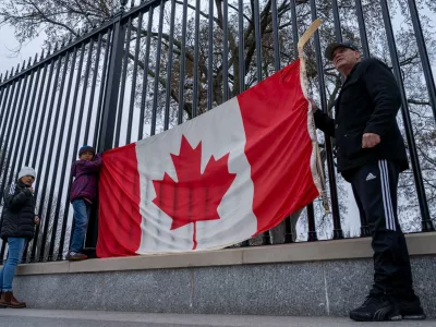 FILE - From right, Toronto residents Douglas Bloomfield, his son Phoenix and wife Ame, who are on vacation in Washington, hold a Canadian flag and an ice hockey stick to show their support for Canada regarding trade tariffs, in front of the White House in Washington, March 13, 2025. (AP Photo/Ben Curtis, File)
