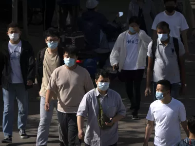 Commuters wearing face masks walk along a street during the morning rush hour in Beijing, Tuesday, May 23, 2023. (AP Photo/Mark Schiefelbein)