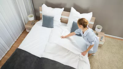Young Female Housekeeper Changing Bedding In Hotel Room