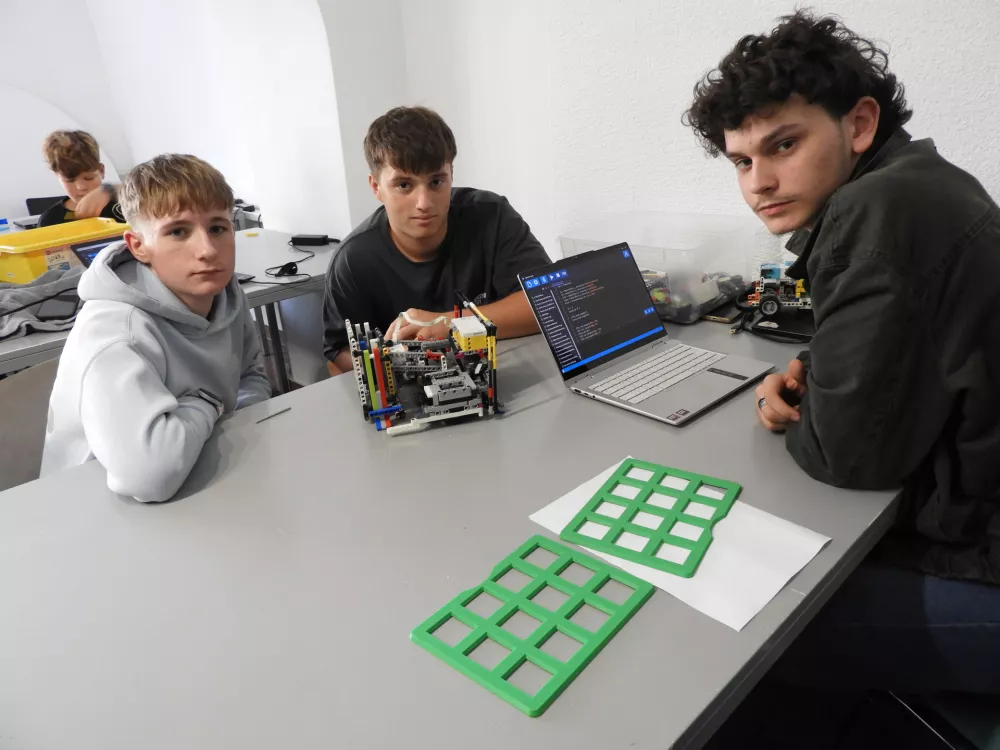 Žan Ker&scaron; (zadaj levo), Nik Bračun (spredaj) in Jakob Golob (desno) bodo tekmovali v najstarej&scaron;i kategoriji. Robot je, kot pove Žan, ki ima vlogo mehanika, že stoodstotno pripravljen na olimpijado, medtem ko ga je potrebno programsko &scaron;e izpiliti, doda Jakob, programer v ekipi. / Foto: Katja Petrovec