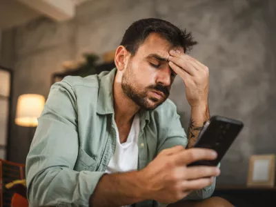 Portrait of adult furious man sit on chair and text sms on cellphone