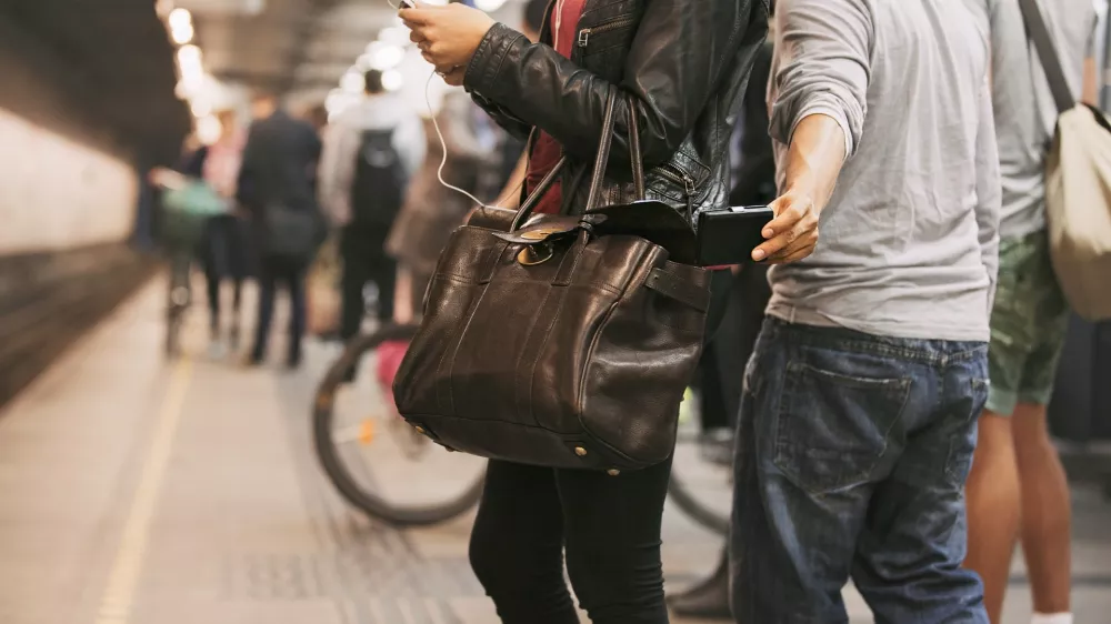 Thief stealing wallet from purse of a woman using mobile phone at the subway station. Pickpocketing at subway station