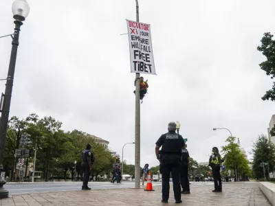 A protester scales a light pole and unfurls a banner to protest the upcoming State Visit by China's President Xi Jinping, Tuesday, Sept. 22, 2026, in Washington. (AP Photo/Allison Robbert)