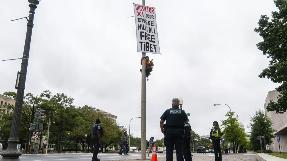 A protester scales a light pole and unfurls a banner to protest the upcoming State Visit by China's President Xi Jinping, Tuesday, Sept. 22, 2026, in Washington. (AP Photo/Allison Robbert)