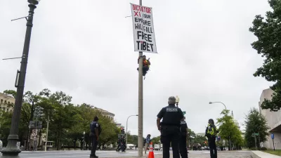 A protester scales a light pole and unfurls a banner to protest the upcoming State Visit by China's President Xi Jinping, Tuesday, Sept. 22, 2026, in Washington. (AP Photo/Allison Robbert)