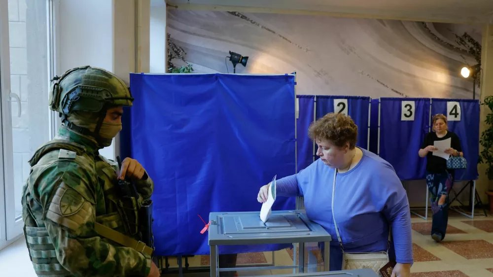 A woman casts her ballot next to a serviceman securing a poling station during Russia's parliamentary elections, in the course of Russia-Ukraine conflict in Donetsk, Russian-controlled Ukraine, September 18, 2026. REUTERS/Alexander Ermochenko