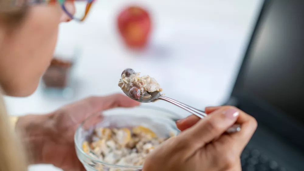 The perfect balance of work and wellness as a woman embraces healthy eating at her workplace. With a bowl of nutritious muesli and yogurt in her hand, optimizing her productivity / Foto: Microgen Getty Images