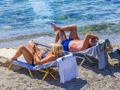 Kos. Greece. July.08.2025. Beautiful view of senior couple relaxing on beach loungers near Aegean Sea enjoying sunny summer day.