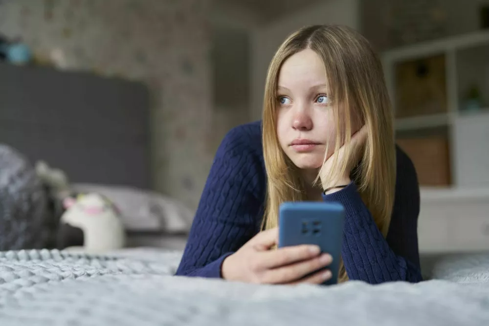 Unhappy Teenage Girl With Mobile Phone Lying On Bed At Home Anxious About Social Media Online Bullying And Using Phone Too Much / Foto: Daisy-daisy