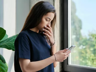 Serious sad teenage female standing at home reading texting on smartphone, copy space. Social life, communication, study education, lifestyle technology concept / Foto: Valeriy_g