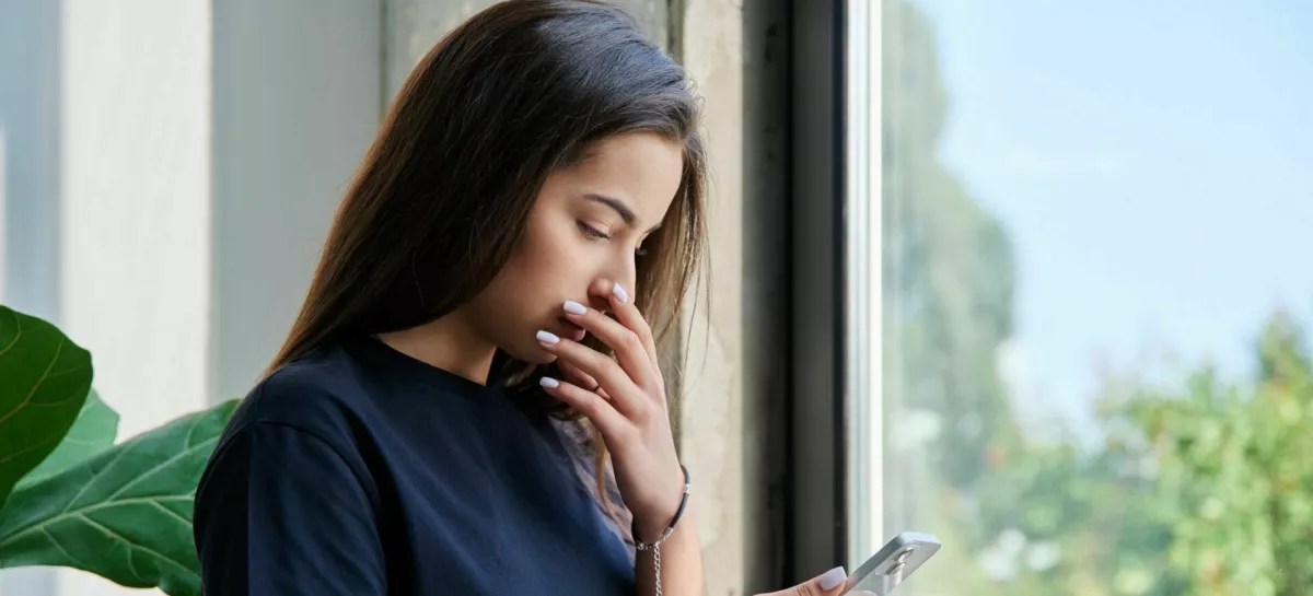 Serious sad teenage female standing at home reading texting on smartphone, copy space. Social life, communication, study education, lifestyle technology concept / Foto: Valeriy_g