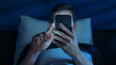 Close up of young man, alone in the dark bedroom, holds his smartphone close to face while scrolling social media or texting late at night. Screen dependence, excessive consumption of content