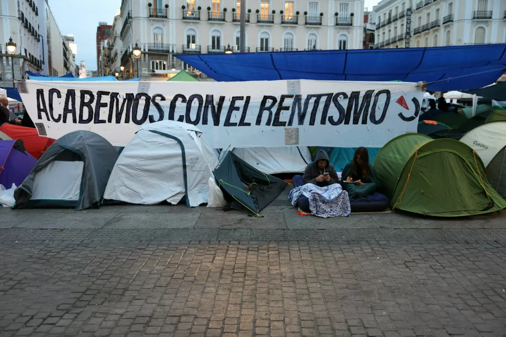 Demonstrators sit next to tents and a banner that reads "Let's put an end to rent-seeking", after setting up a camp at Puerta del Sol square in protest against Spain's housing crisis after the forceful eviction of an 87-year-old woman from her apartment in Madrid, Spain, September 28, 2026. REUTERS/Juan Medina