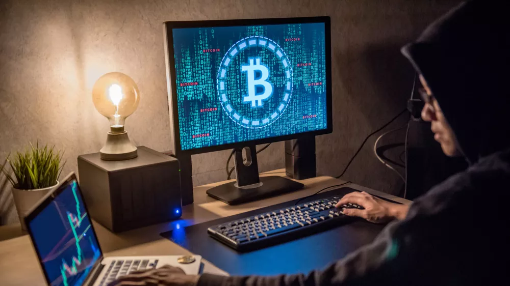 Hacker man using laptop and computer with Bitcoin green binary graphic and cryptocurrency candlestick graph price on monitor screen. Cyber crime digital currency laundering concept
