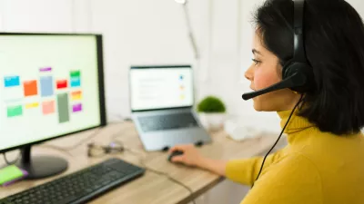 Latin freelancer wearing wireless headset typing on laptop, managing remote project and providing customer support from home workspace