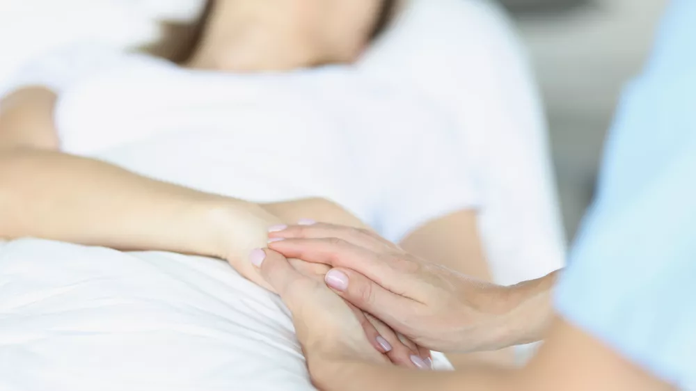 On bed lies a sick doctor sitting next to him and sympathetically holds hand. Euthanasia in world practice concept