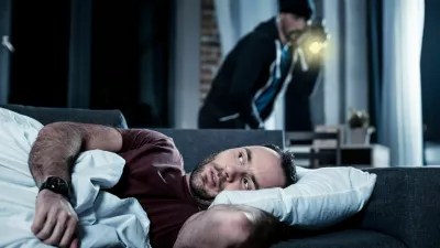 Breaking into house. Alarmed disturbed bearded man waking up and hearing someone being in his house and a criminal with a torch standing behind him / Foto: Zinkevych