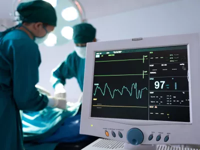Selective at monitor and nurse using defibrillator to pump at chest of unconscious with low heart rate patient to save life while doing medical surgery inside of operating room. Emergency CPR.