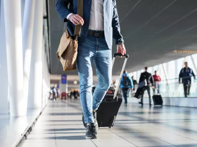 Man with shoulder bag and hand luggage walking in airport terminal, photo with men's legs walking in airport terminal
