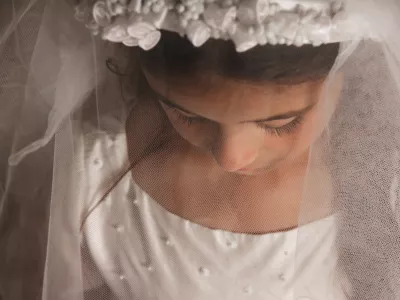 A young girl preparing for her holy communion, photographed with her veil covering her face and looking down
