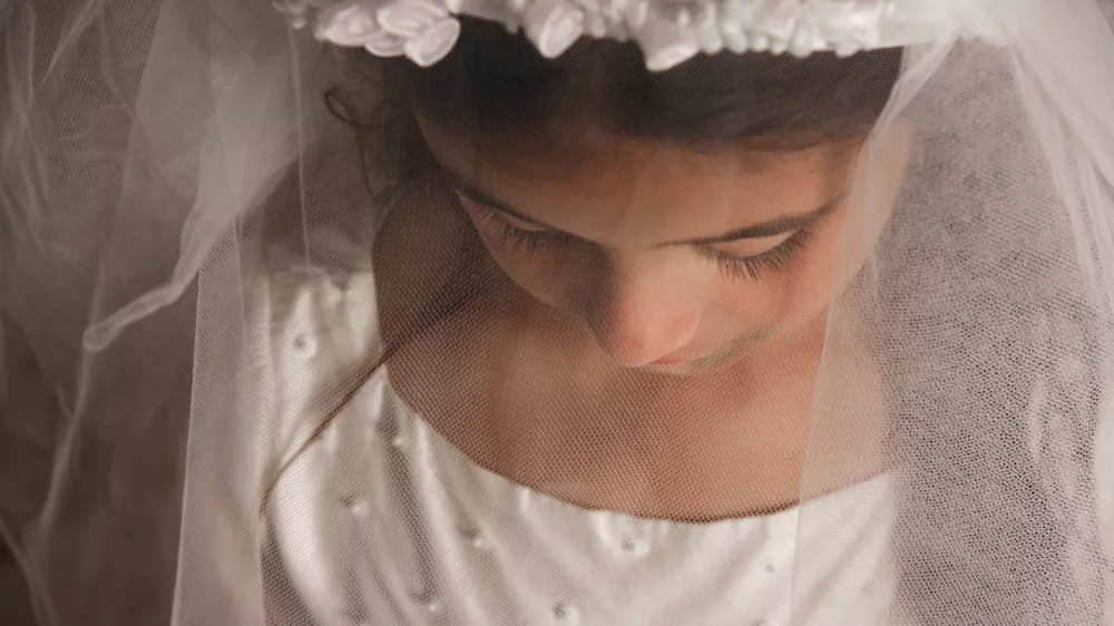 A young girl preparing for her holy communion, photographed with her veil covering her face and looking down